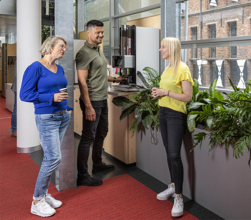 Drie collega's staan te praten bij het koffieautomaat